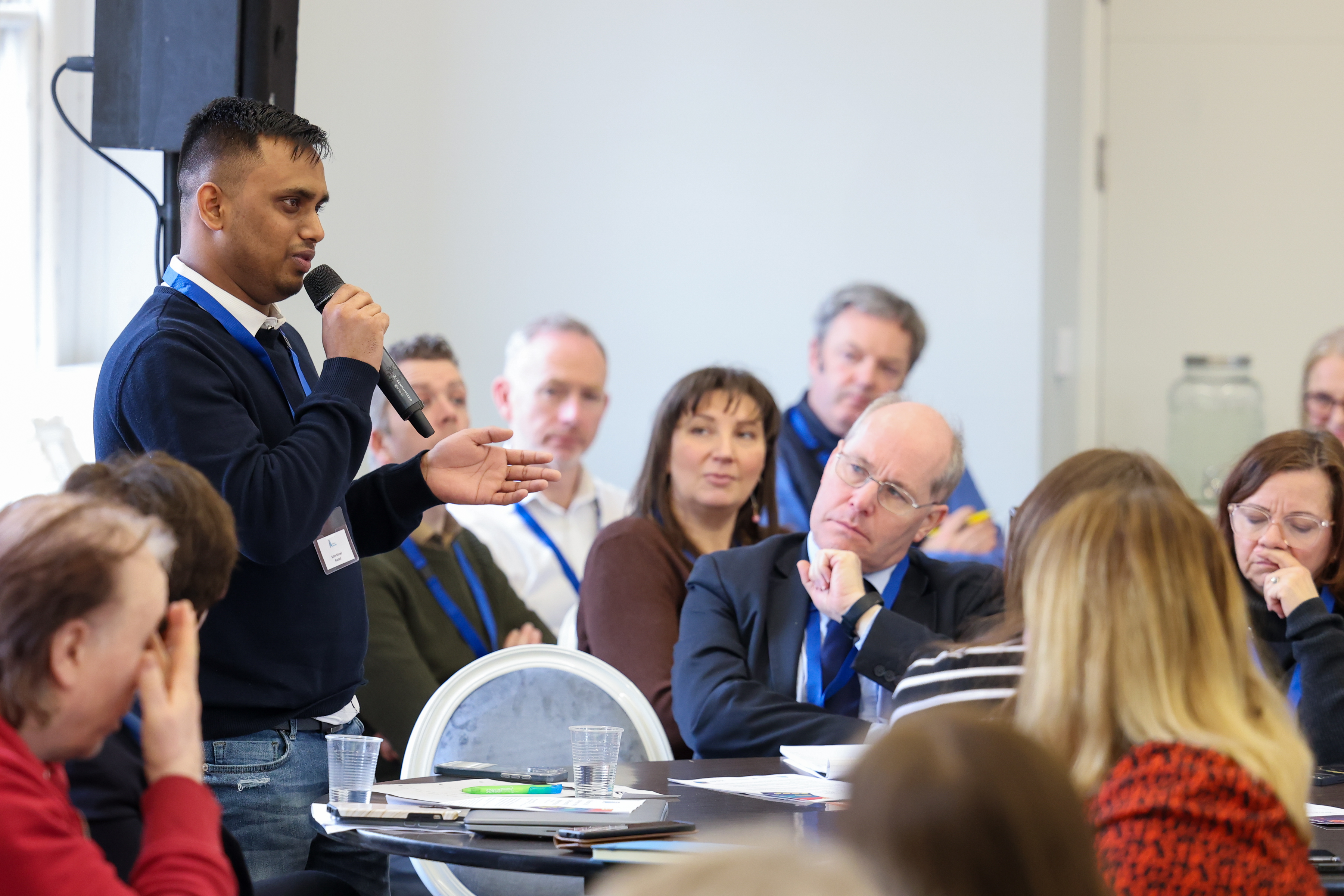 Adult learner Sultan Ahmed holding a microphone speaking to an audience at our Who Does It Cost policy discussion on Monday 4 March  